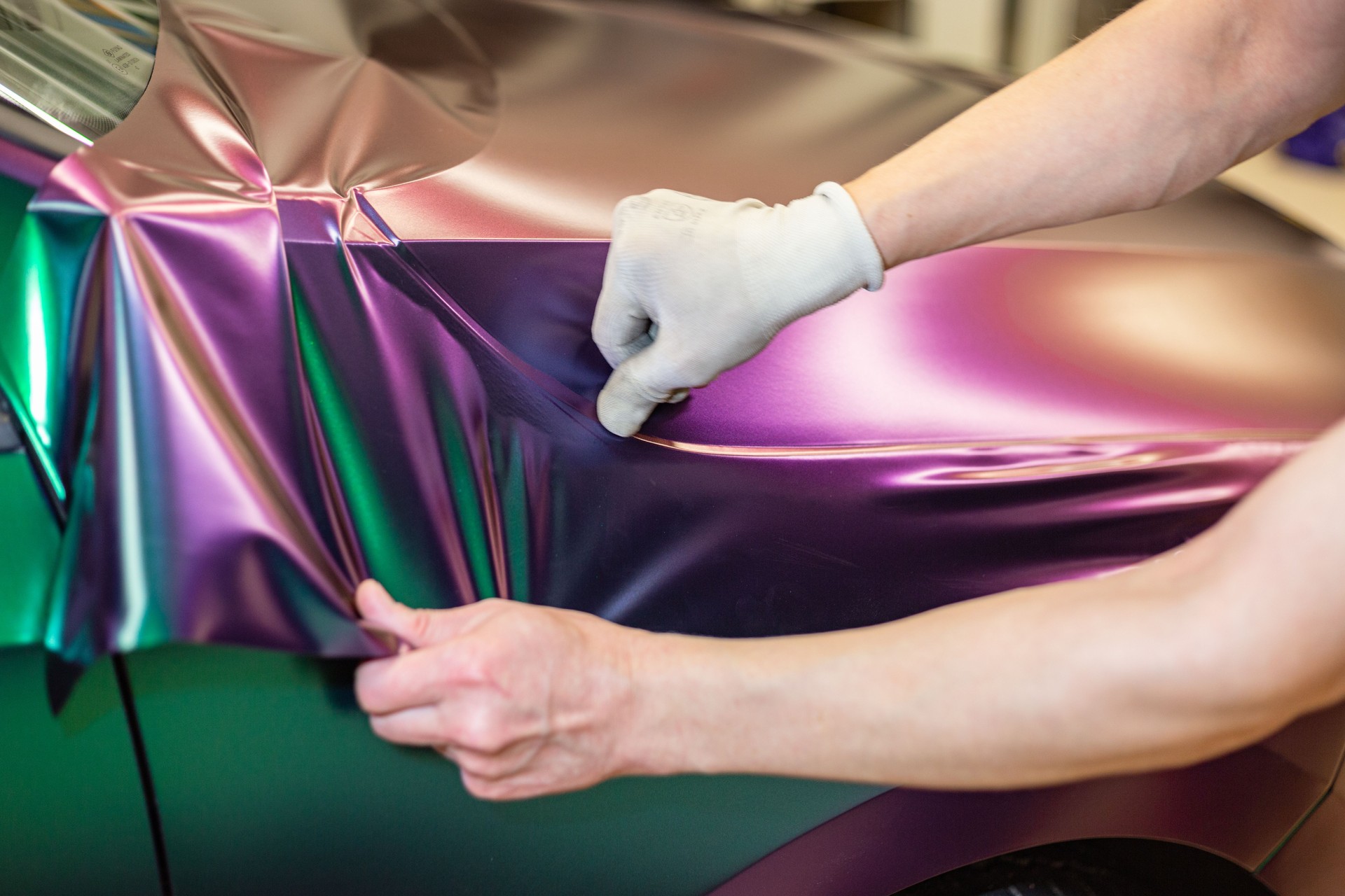 A specialist in wrapping a car with chameleon-colored vinyl film in the process of work. Car wrapping specialists cover the car with vinyl sheet or film.
