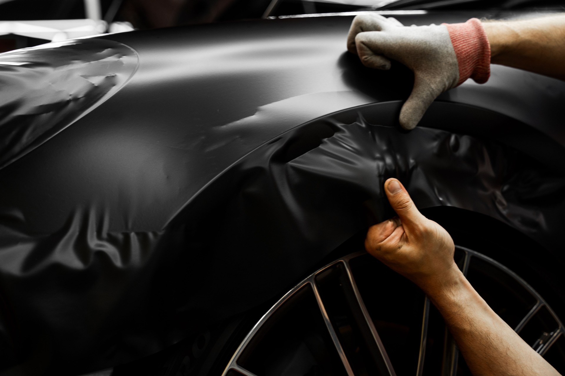 Matte black vinyl wrapping around car with smooth alignment over curves and edges. Matte black vinyl wrap application on front fender and wheel arch of luxury vehicle. Vinyl Wrapping of Car.